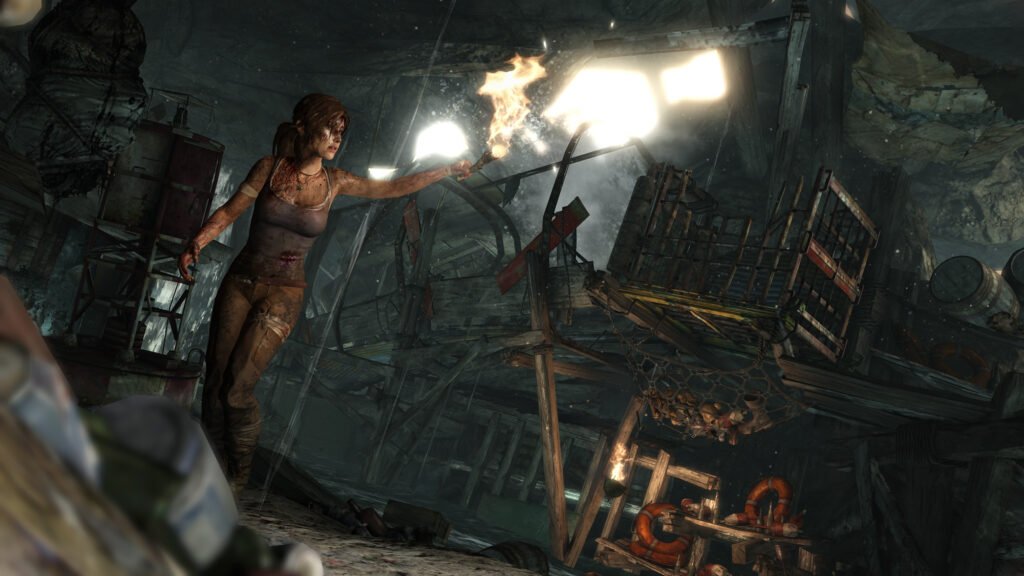 Lara Croft ferida e suja segurando uma tocha num navio naufragado, no Tomb Raider de 2013